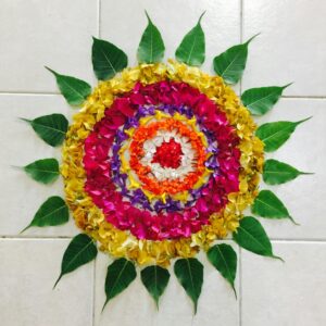 A vibrant floral mandala made of colorful petals and green leaves arranged on a tile floor.